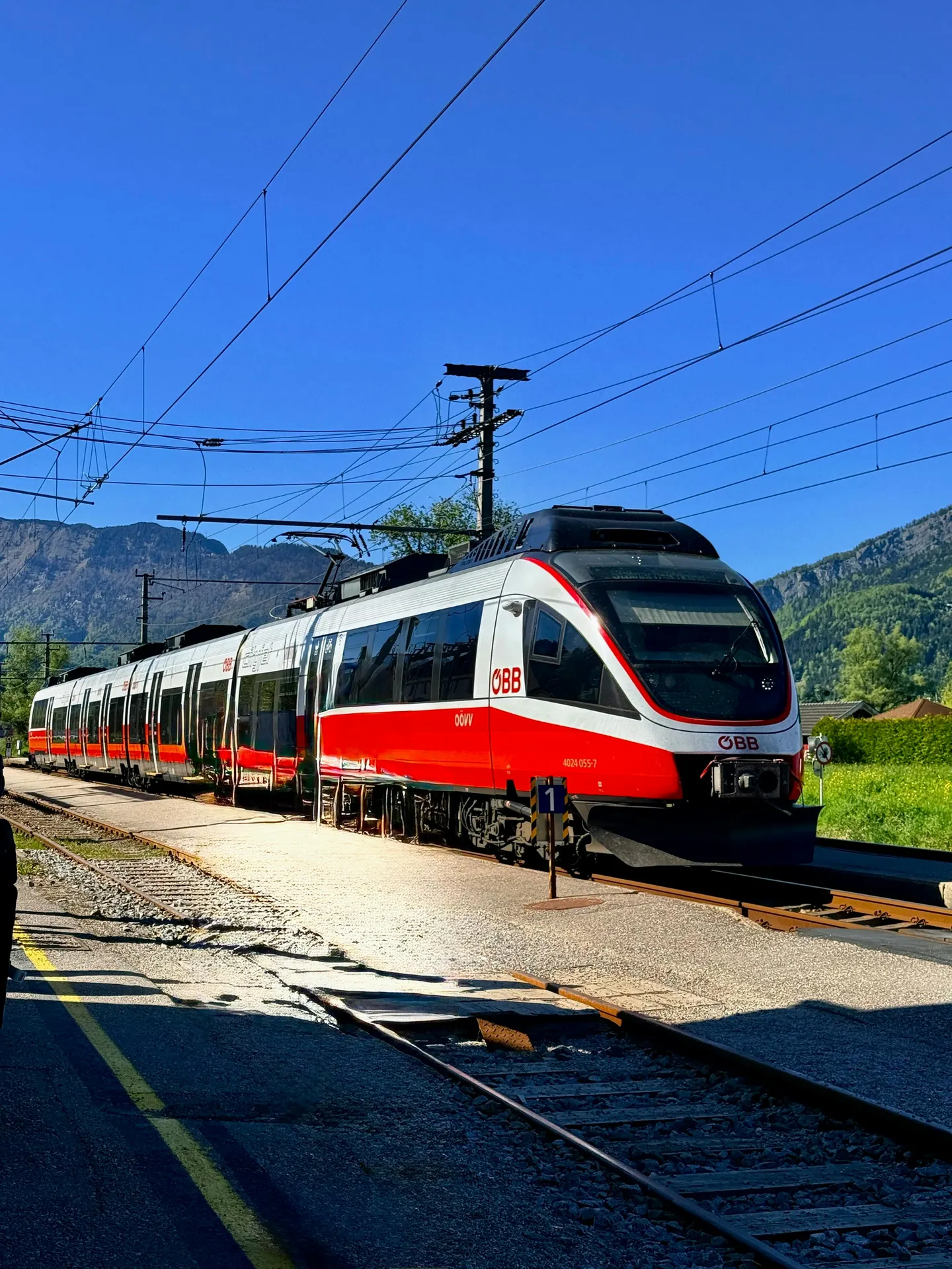 Eleganter österreichischer Zug vor Alpenkulisse und historischem Bahnhof